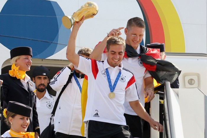 DFB Kapitän Philipp Lahm (C) hält den Welmeisterpokal 2014, Bastian Schweinsteiger ist ebenso wie Samy Khedira zu sehen beim Ausstieg in Berlin-Tegel. AFP PHOTO / POOL / KARINA HESSLAND / AFP / POOL / KARINA HESSLAND