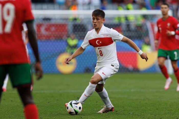 Der türkische Nationalspieler Arda Güler mit der Rückennummer 8 am Ball im weißen Nike-Trikot der türkischen Nationalmannschaft. Im Hintergrund ist Cristiano Ronaldo im roten Portugal-Dress zu erkennen. Das Bild zeigt das neue Nike-Trikot der Türkei vor der WM 2026. (Copyright Depositphotos.com)