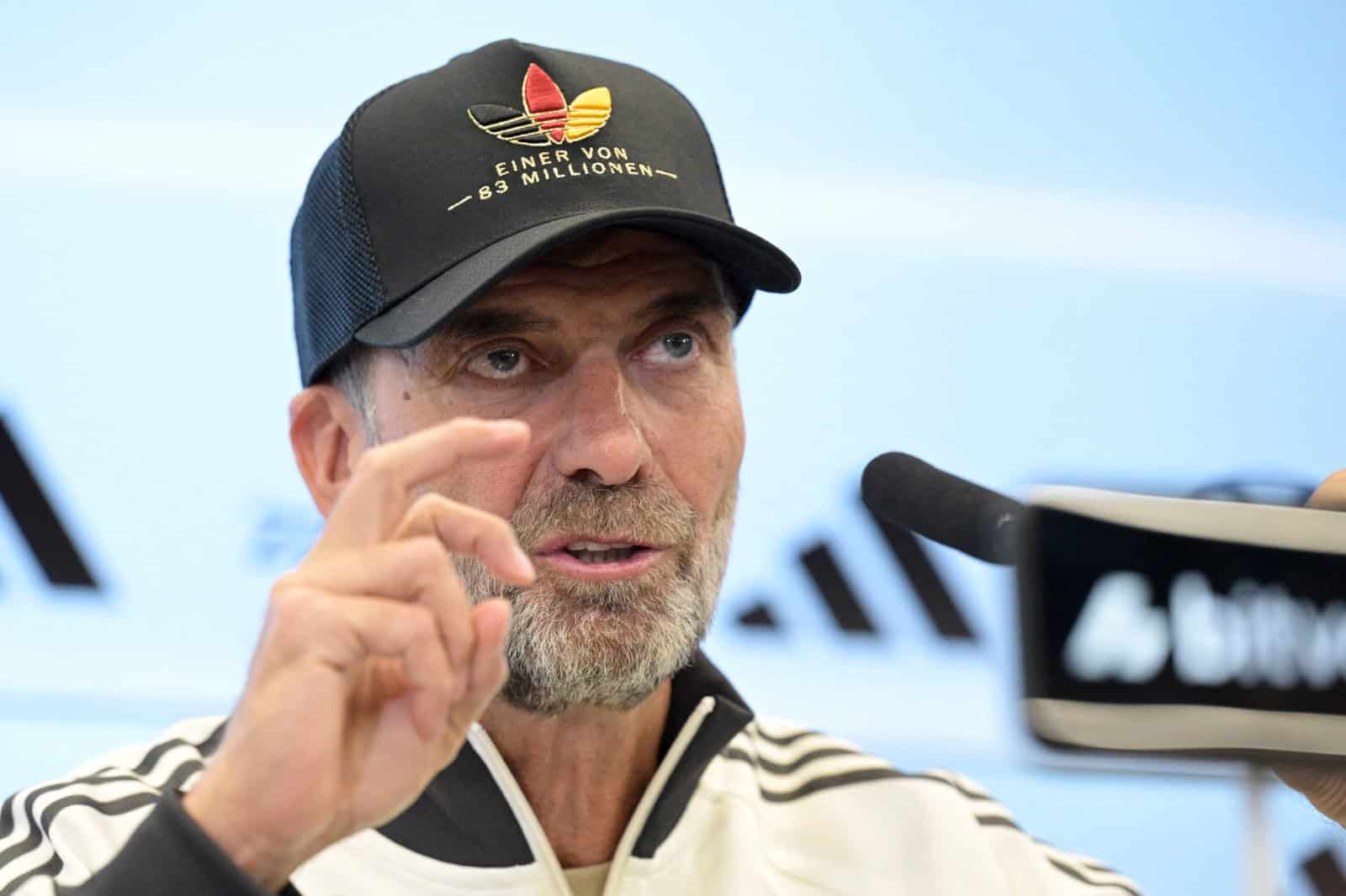 Jürgen Klopp gestikuliert bei der Pressekonferenz zur Nominierung seines ersten DFB-Kaders am 17. September 2026 in Frankfurt am Main. Auf dem Kopf die Kappe „Einer von 83 Millionen“, die adidas nun in den Handel bringt. (Foto: Hannes P. Albert / AFP)