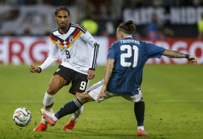 Kevin Schade kämpft beim Nations-League-Spiel zwischen Deutschland und Griechenland am 27. September 2026 in Augsburg mit Konstantinos Tsimikas um den Ball. (Copyright AFP/Michaela Stache)